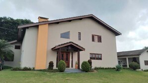A two-story house with a beige exterior, a brown roof, and a small porch with a wooden door. - Excellent Country House (Água Preta)