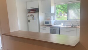A kitchen with white cabinets, a microwave, a sink, and a window with a view of greenery. - Port Willunga House on the Fleurieu Peninsula (Port Willunga)