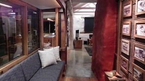 A narrow hallway with a wooden floor, a grey sofa with a pillow, and a red curtain. - Barakee Creek - The Old Shack (Cattai)