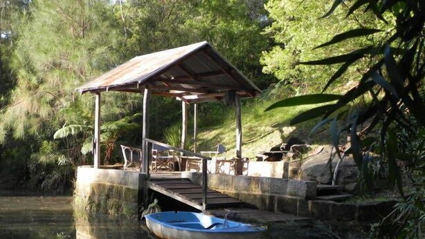 A wooden dock extending into a calm body of water, with a small boat tied to it. - Barakee Creek - The Old Shack (Cattai)
