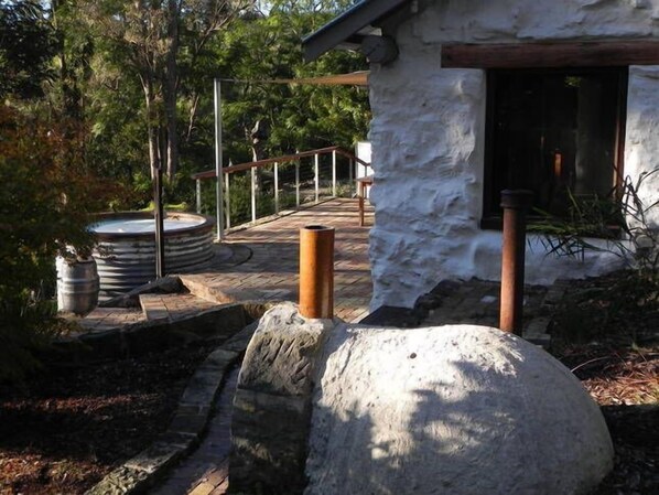 A stone pathway leading to a rustic building with a wooden deck and a hot tub.