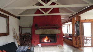 A cozy living room with a fireplace, a sofa, and a dining area with a table and chairs. - Barakee Creek - The Old Shack (Cattai)