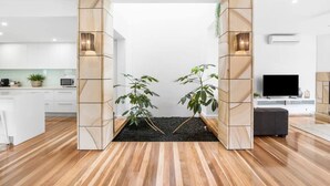 A modern living room with a wooden floor, a TV, and a plant arrangement. - Luxury Townhouse 150 metres to the beach (Torquay)