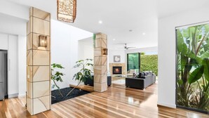 A modern living room with a fireplace, a large window with a view of greenery, and a wooden floor. - Luxury Townhouse 150 metres to the beach (Torquay)