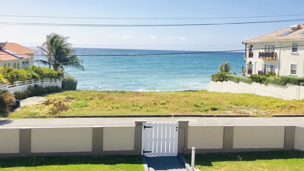 A coastal view with a white gate leading to a property with a red roof and a balcony.
