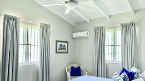 A bedroom with a bed, a chair, a ceiling fan, and an air conditioning unit.