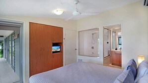 A bedroom with a bed, a wooden wardrobe, a ceiling fan, and a shower area. - Oasis 23, Seaview Apartment on Hamilton Island (Hamilton Island)