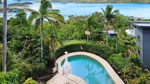A pool surrounded by lush greenery and a view of the sea. - Oasis 23, Seaview Apartment on Hamilton Island (Hamilton Island)
