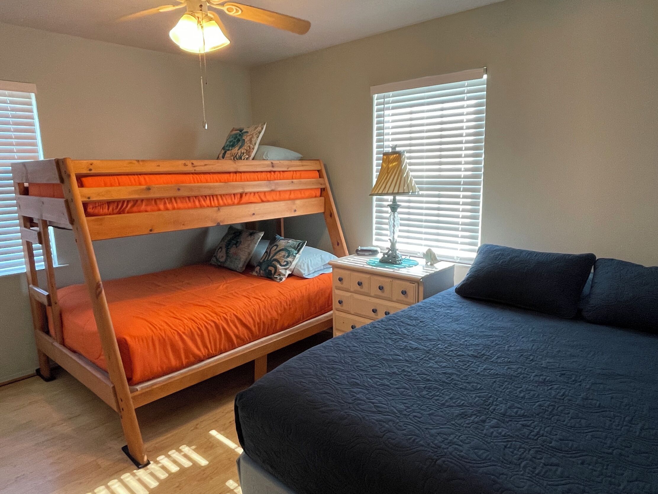 A bedroom with a bunk bed, a single bed, a nightstand, a lamp, and a ceiling fan.