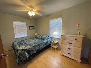 Relax in this serene bedroom with a comfortable bed, ceiling fan, and natural light pouring in through the windows.
