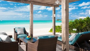 Un espacio de estar techado al aire libre con mobiliario de mimbre, una mesa con un frutero, y vistas a la playa y al océano.