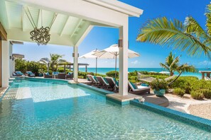 A pool area with clear blue water, lounge chairs, umbrellas, and a view of the ocean.