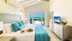 Un dormitorio con cama, televisión, cómoda y vista al océano a través de una puerta corrediza.