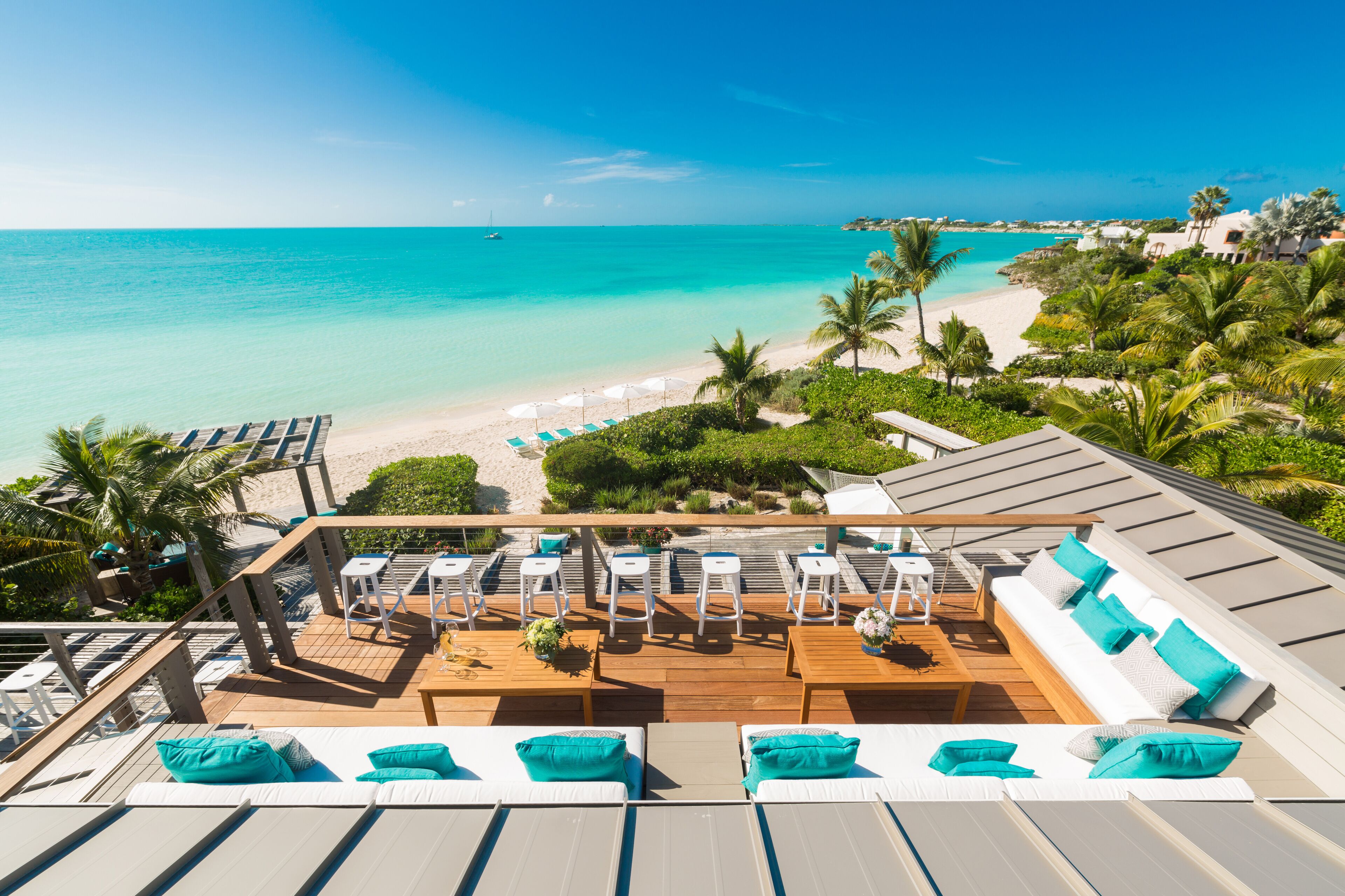 A rooftop terrace with a view of a beach and ocean, furnished with lounge chairs and a sofa.