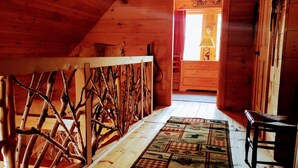 Interior de madera con techo inclinado, barandilla de madera, alfombra estampada y una pequeña silla de madera.