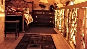 Un dormitorio acogedor en el ático con techo de madera, una cama, un tocador y una ventana con vistas a árboles.