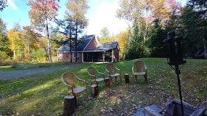 Une cabane rustique dotée d’un porche, entourée d’une cour verdoyante et d’arbres.