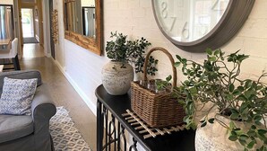 Un pasillo con un gran reloj de pared, un espejo, una cesta de mimbre y una planta en maceta.
