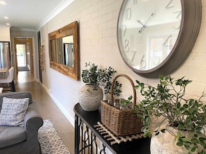 A hallway with a large wall clock, a mirror, a wicker basket, and a potted plant.