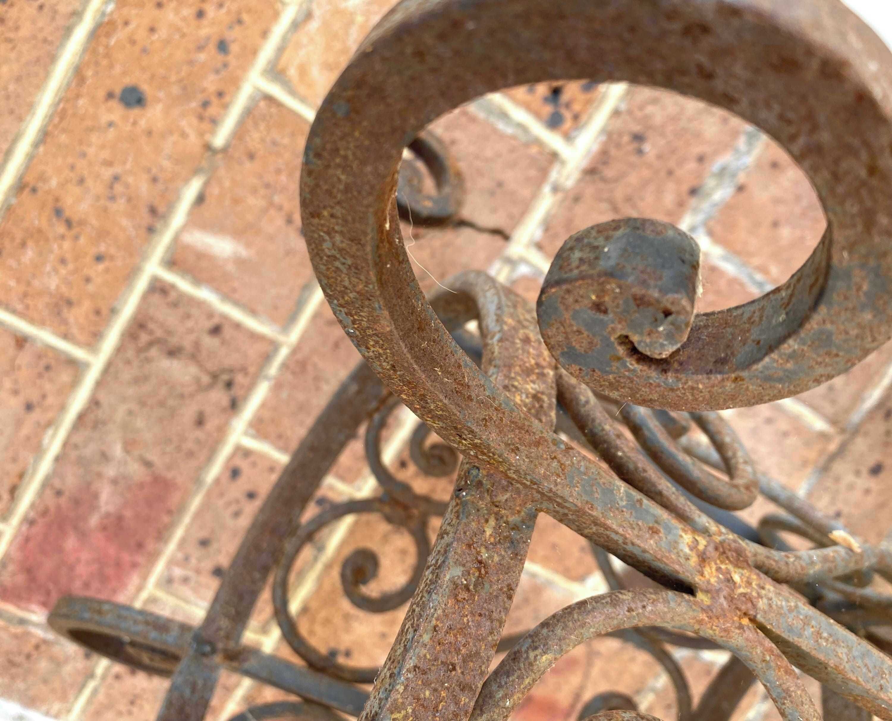 Ein Detailaufnahme einer verrosteten Metallstruktur mit spiralförmigem Design vor einer Backsteinwand.