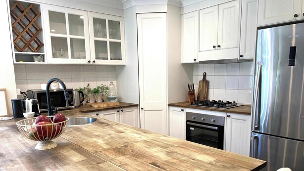 Una cocina con armarios blancos, una isla de madera, electrodomésticos de acero inoxidable y un bol de fruta.