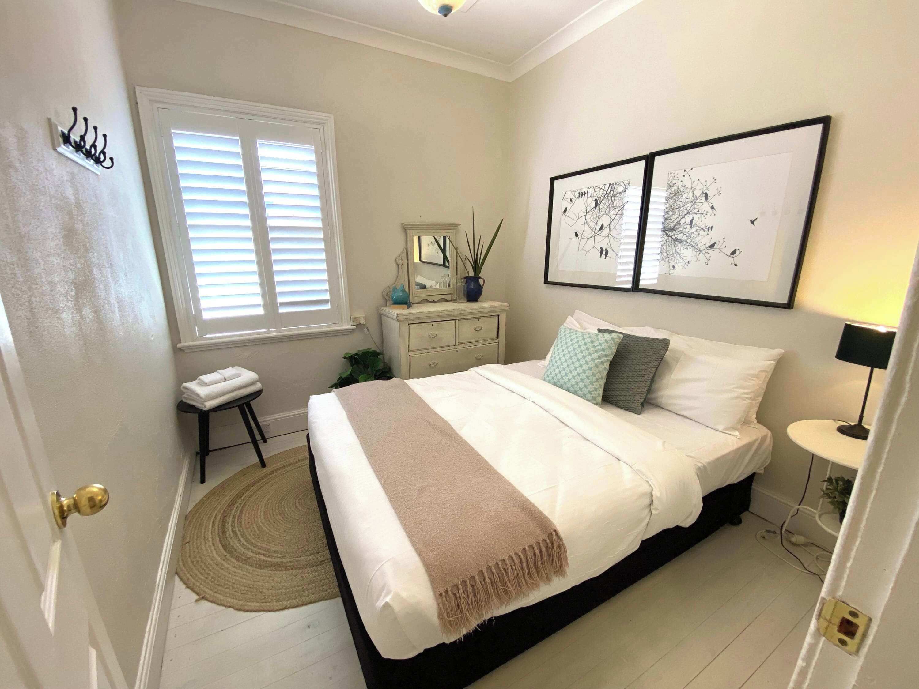 A bedroom with a bed, bedside table, lamp, window, and artwork on the wall.