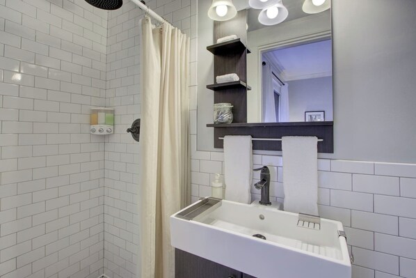A modern bathroom with a white sink, a mirror with lights, and a shower curtain.
