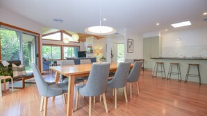 A modern kitchen with a central island, a dining area with a wooden table and grey chairs, and a living area with a sofa and a TV. - ON THE TRAIL : Bright (Bright)