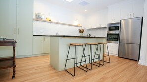 A modern kitchen with white cabinets, a stainless steel refrigerator, and wooden bar stools.