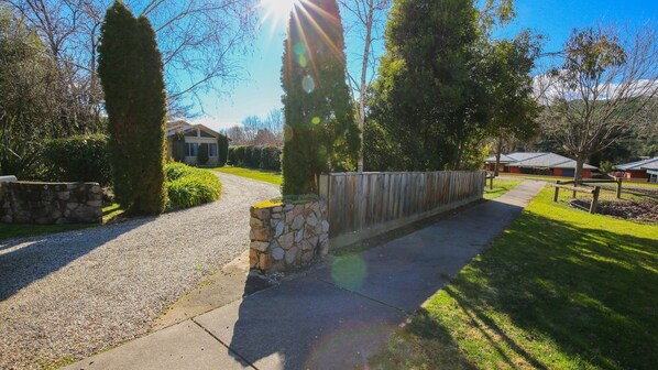 A residential driveway with a stone wall, a wooden fence, and a well-maintained lawn. - ON THE TRAIL : Bright (Bright)