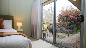 A hotel room with a bed, a nightstand, a lamp, and a sliding glass door leading to an outdoor deck with a chair and a table.