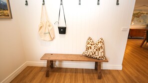 A wooden bench with patterned pillows against a white wall with vertical paneling. - ON THE TRAIL : Bright (Bright)
