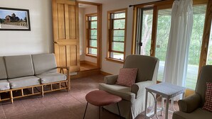A cozy room with a wooden door, a cushioned sofa, a small table, and a view of greenery outside. - Tranquil Views of Drummer Cove (1321) (Wellfleet)