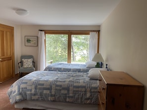 Quarto com duas camas, uma cadeira, cômoda e janela com cortinas.