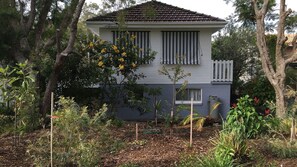 A two-story house with a grey exterior and a tiled roof, surrounded by a garden with various plants and trees. - Lemon Tree Shack - Family friendly by the sea (Lemon Tree Passage)