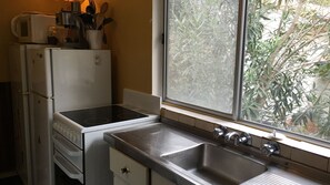 A compact kitchen with a built-in stove, a sink, and a window overlooking greenery. - Lemon Tree Shack - Family friendly by the sea (Lemon Tree Passage)