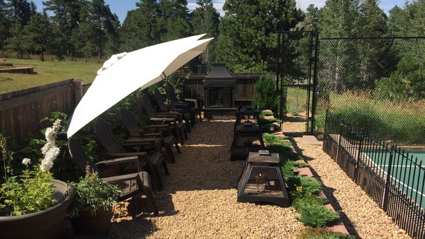 An outdoor seating area with wooden chairs and a large white umbrella, surrounded by gravel and potted plants. - Experience a Relaxing Retreat at Lookout Mountain Lodge (30 Day Min) (Golden)