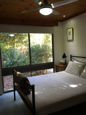 A bedroom with a bed, a nightstand, a ceiling fan, and a window with a view of greenery. - Corkwood at Smiths Lake - 3 bedroom pet friendly (Smiths Lake)