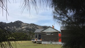 Eine rustikale Holzhütte mit Metalldach und Holzwänden, gelegen in einer grünen Wiese mit Bergen im Hintergrund.