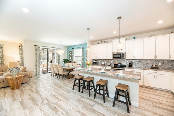 A modern kitchen with white cabinets, a granite countertop, and a central island with stools. - 🏖️ Solterra Beach - 6BR Home with Pool, Spa & Resort Perks (Davenport)