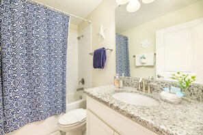A bathroom with a white toilet, a bathtub, and a sink with a granite countertop. There is a starfish decoration on the wall and a towel rack with towels. - 🏖️ Solterra Beach - 6BR Home with Pool, Spa & Resort Perks (Davenport)