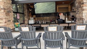 Een buitengebied met een bar, vier Adirondack stoelen, een toonbank met een menu en een groot scherm waarop evenementinformatie wordt getoond.