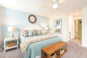 A bedroom with a bed, two bedside tables, a bench, a ceiling fan, and a wall with a mirror and artwork. - 🏖️ Solterra Beach - 6BR Home with Pool, Spa & Resort Perks (Davenport)