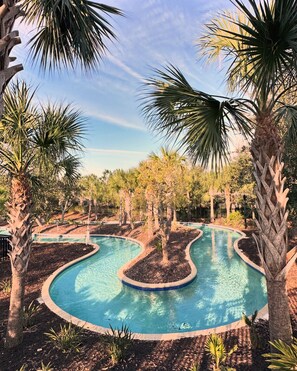 A swimming pool with a wavy edge, surrounded by palm trees and other vegetation. - 🏖️ Solterra Beach - 6BR Home with Pool, Spa & Resort Perks (Davenport)