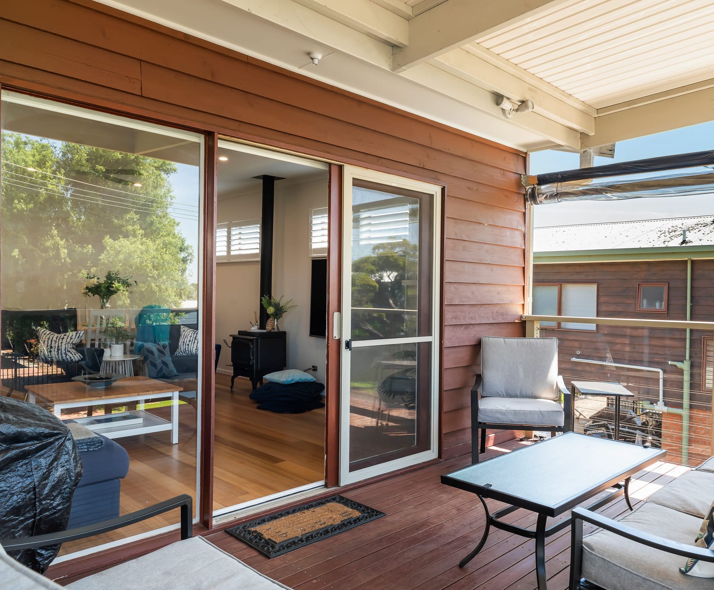 A covered patio area with a sliding glass door leading to a room, a small table, a chair, and a sofa.
