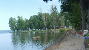 Una playa arenosa con un lago tranquilo al fondo, rodeada de árboles y un paseo de madera.