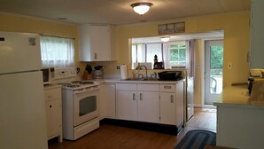 Una cocina compacta con electrodomésticos blancos, un lavamanos pequeño y una ventana con cortinas.