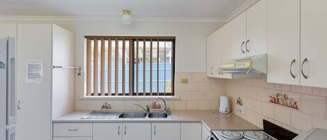 A compact kitchen with a double sink, a stove, and cabinets.