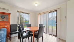 A dining area with a round table and six chairs, a wooden cabinet with drawers, and a view through a sliding glass door to an outdoor area. - Pet Friendly in Port Elliot (Port Elliot)