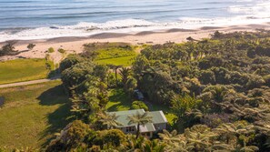Une propriété située sur la côte, avec une maison entourée d’une végétation tropicale luxuriante et une plage en arrière-plan.